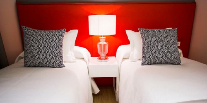 Vista de dormitorio con dos camas individuales y cabecero largo rojo